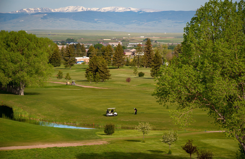 Golfers and a golf cart are shown on a hole of Jacoby Golf Course with the Snowy Mountains in the background.
