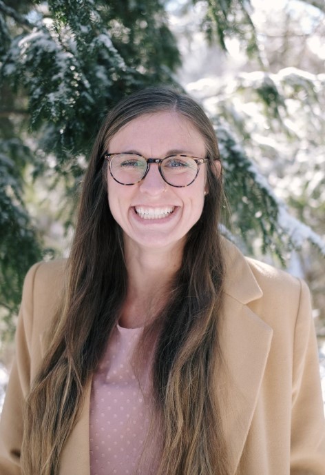 Jennifer Kurtz wearing a tan coat and a pink polka-dot blouse, in the background is a snowy pine tree,