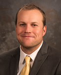 A man wearing a dark gray suit jacket with a yellow tie and white button-up shirt.