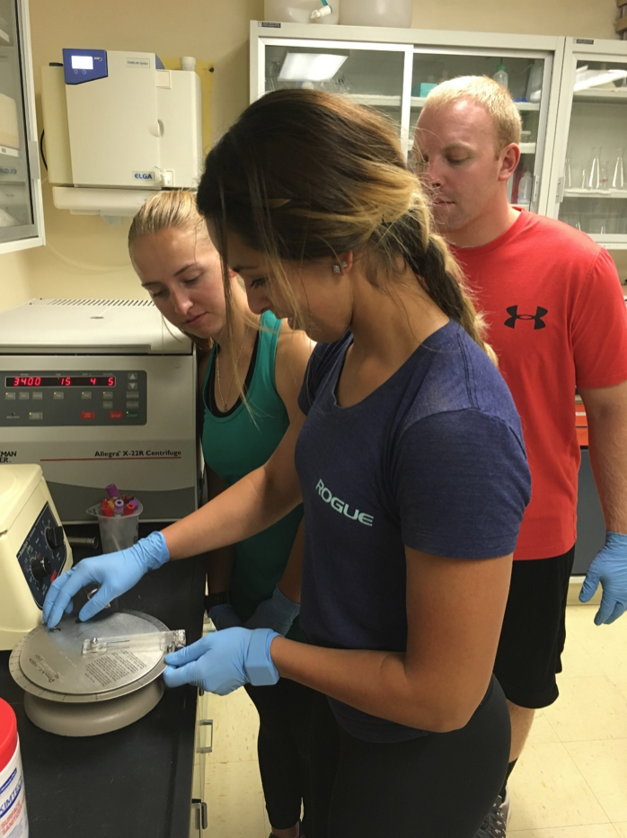 Two female students working on a lab smaple, while a professor looks over their work.