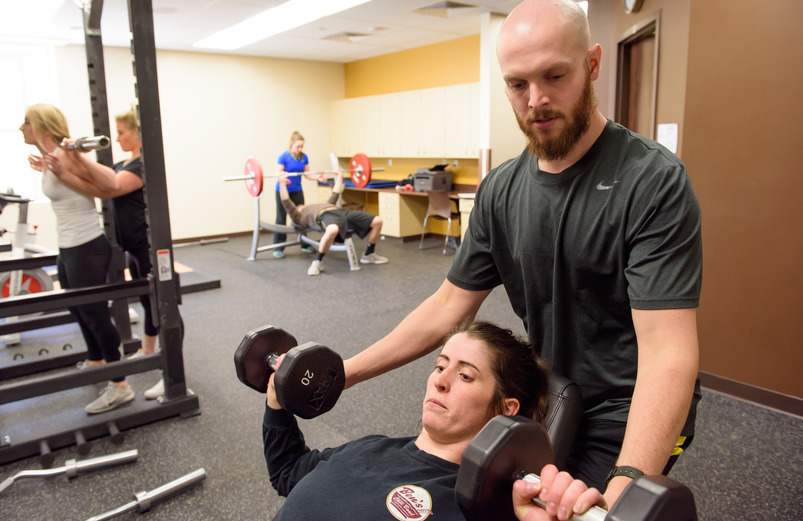 A man helps a person with their form while weight lifting.