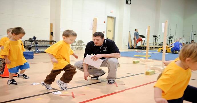 A PE teacher crouched down and directing childern through different exercises.