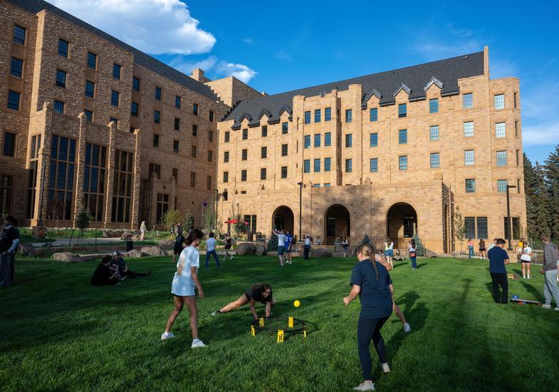 Students in a green space next to a building hanging out and playing lawn games.