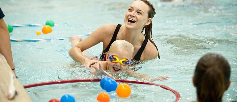 A woman and child play with toys in a pool.
