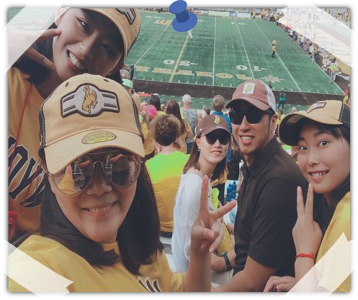 A few people look back at the camera and pose, in the background is a football field.