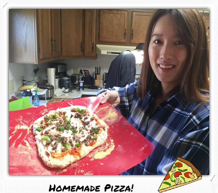 A woman holding up a homemade uncooked pizza.