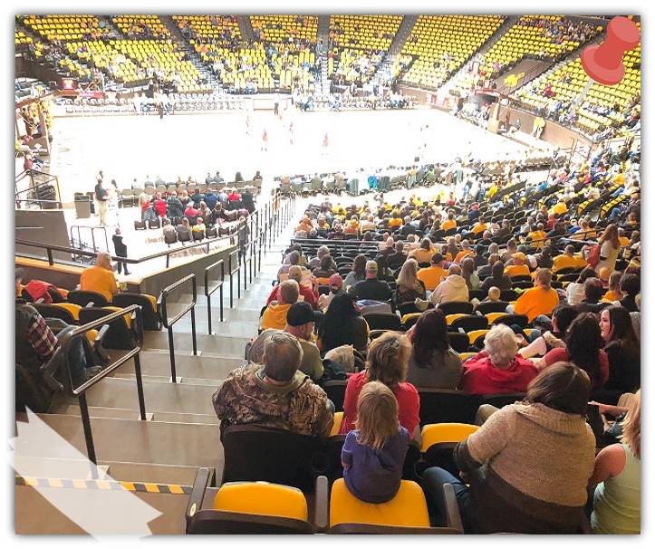 A basketball court and stadium with people sitting and watching the game.