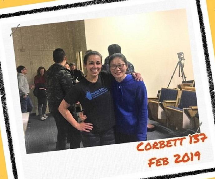 Two people hugging while more people are working on something behind them.