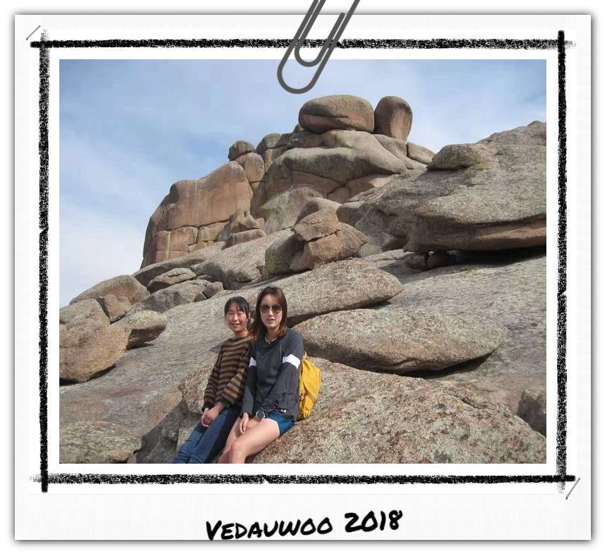 Two women leaning against a large rock outcropping.