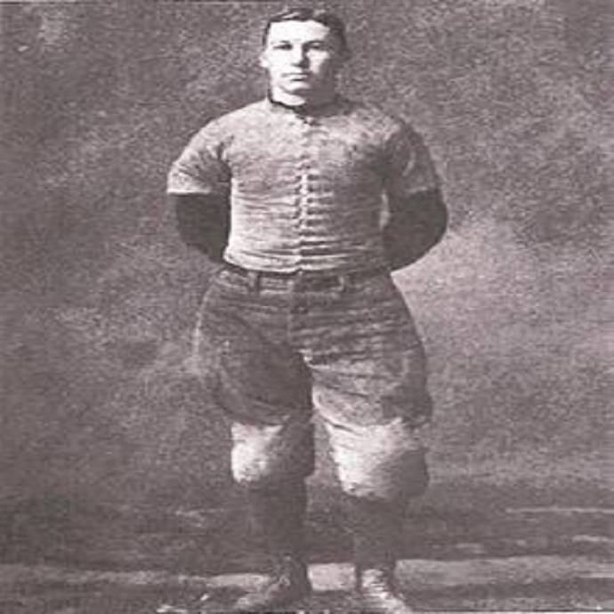 A black and white photo of a young man wearing an old-fashioned football uniform.