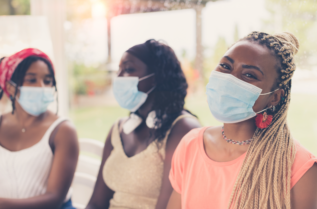Three women wearing face masks, two are talking to each other and the third is looking at the camera.