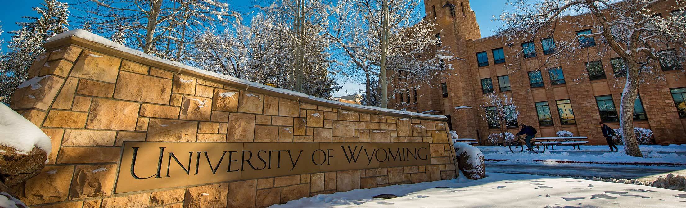 A University of Wyoming stone sign next to a building with snow on the ground.