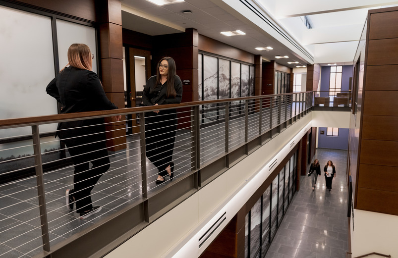 Two law students stand on a balcony talking in the UW college of law building.