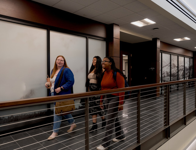 Two law students stand on a balcony talking in the UW college of law building.