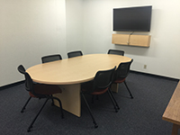 image of room 008, conatining a conference table, six plastic chairs on wheels, and a large wall mounted computer screen