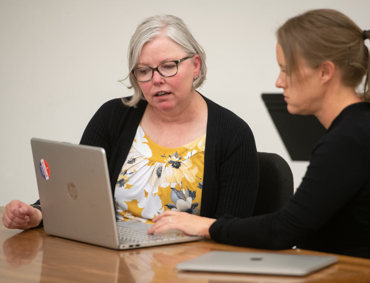 A professor sits with a student with a laptop in front of them.