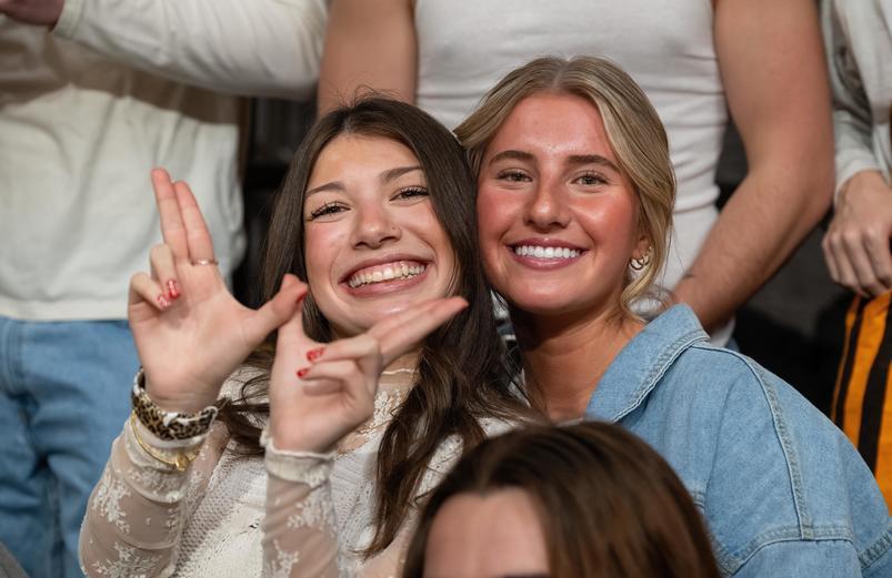 two students smiling, one forming her hands into a W