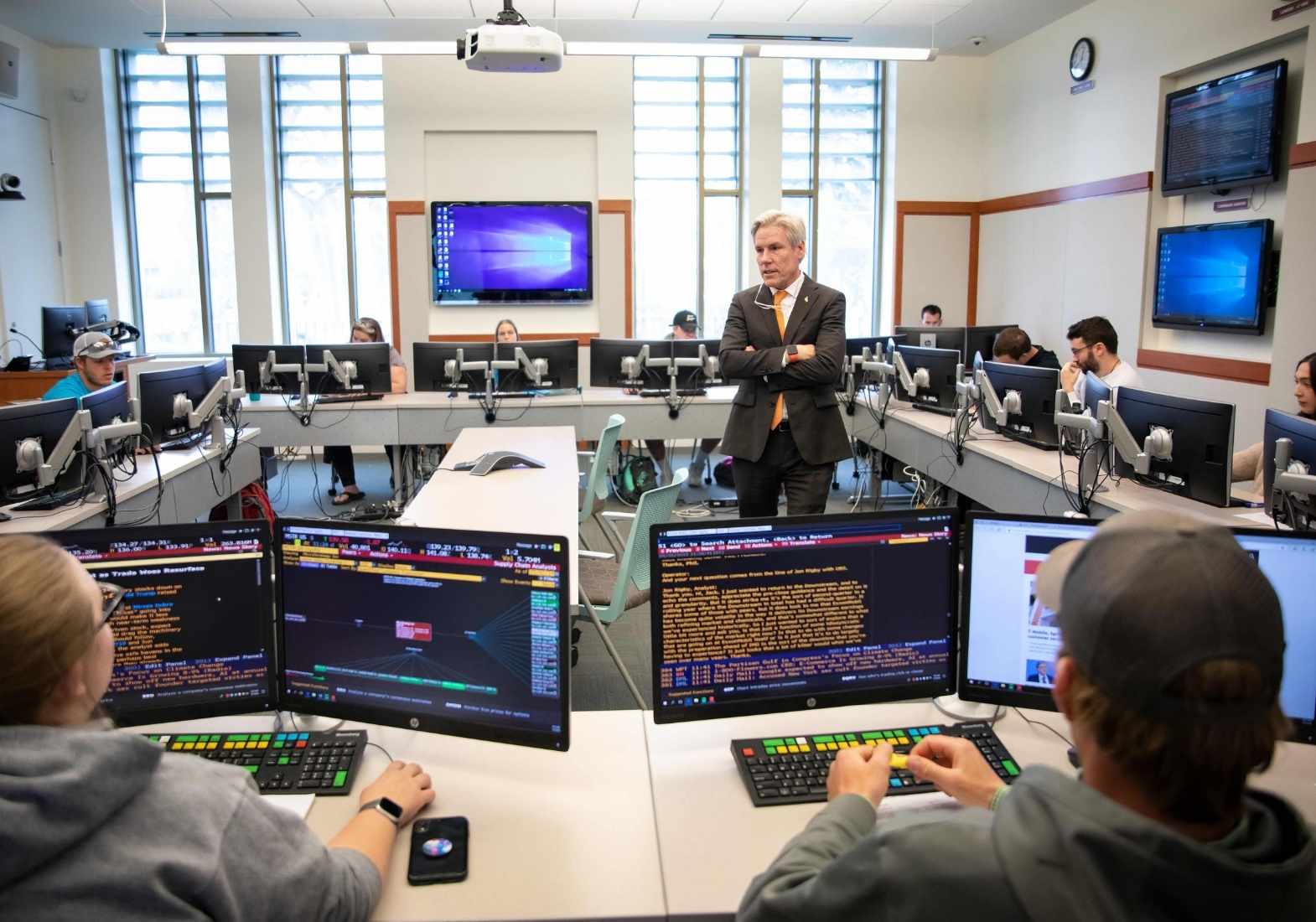 a professor in the middle of a classroom surrounded by students at computers