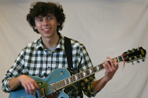 Lex in a flannel shirt holding a guitar