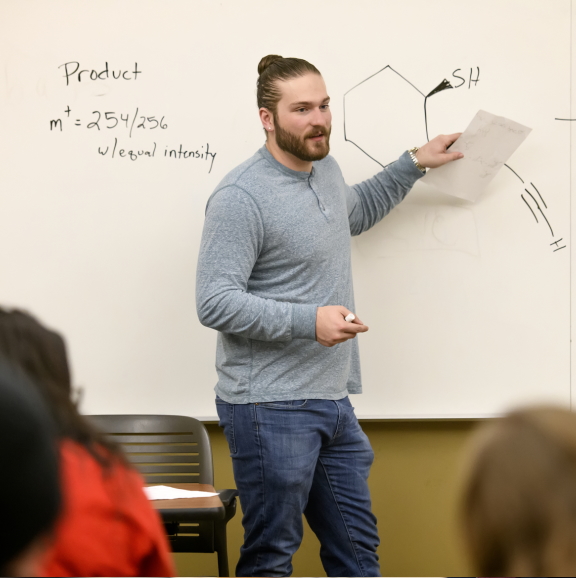 person at front of classroom teaching at a white board