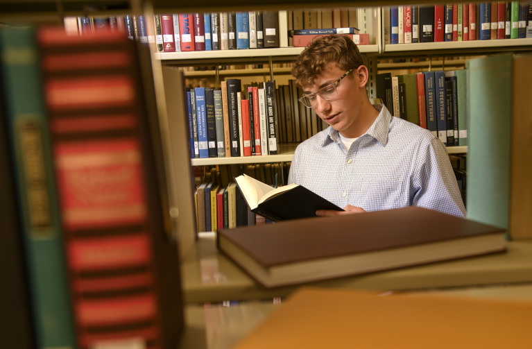 student looking a t book in between the stacks