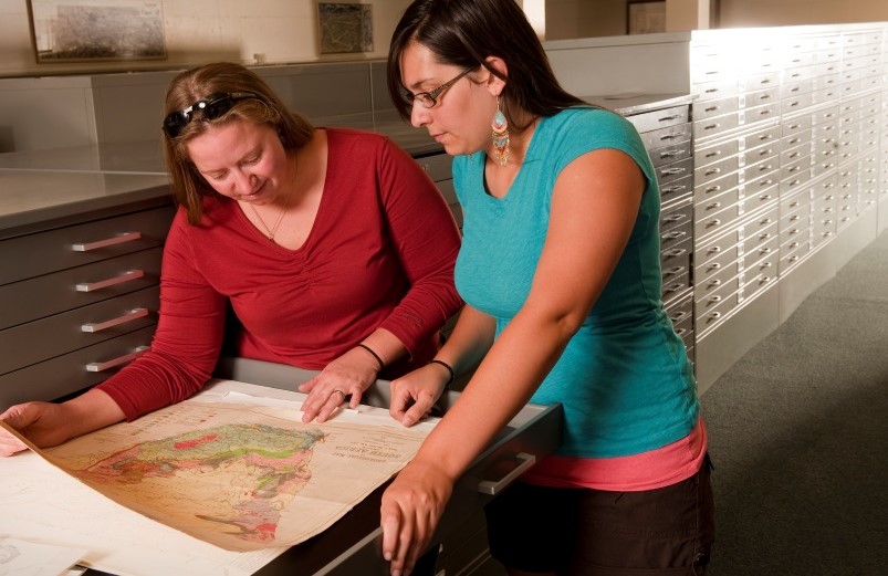 Two people looking at maps in the geology library.