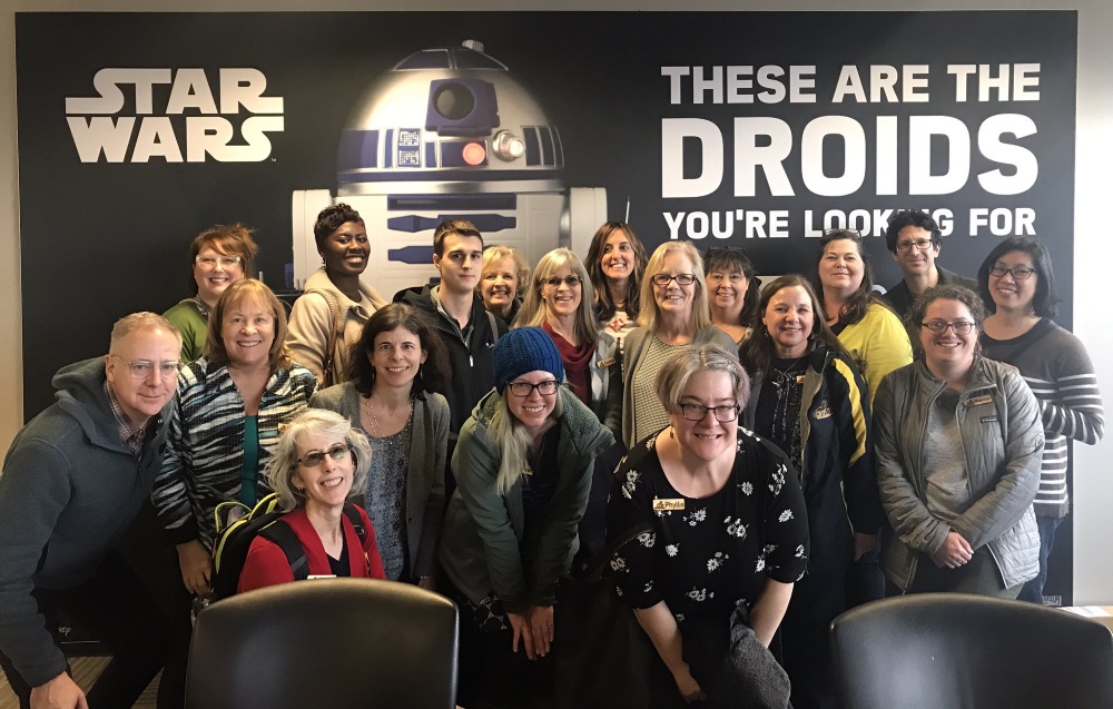 group of people standing in front of a star wars droid graphic