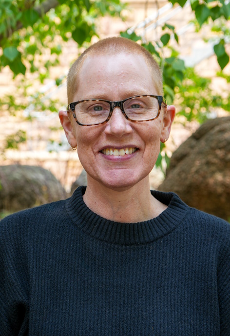 Patricia headshot taken outside. They have a nice smile and are wearing glasses. Taken outside with tress and rocks in the background