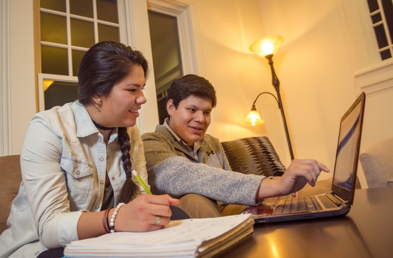 two people sitting in a living room looking at a computer