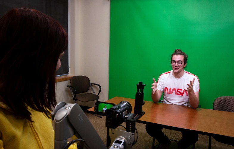 Two students recording in the Studio Coe recording space in front of a green screen.