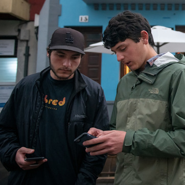Two students look for directions on a phone while standing in a street.