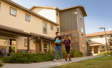 Two students walk on a sidewalk in front of UW's apartment units.