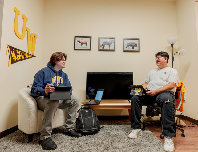 Two UW students sit in chairs and smile at each other in their dorm room that they share in the residence halls