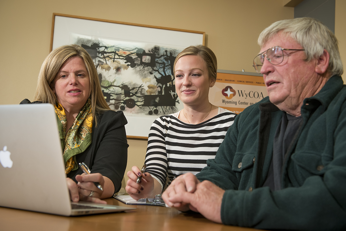 three people looking at a laptop screen and helping each other