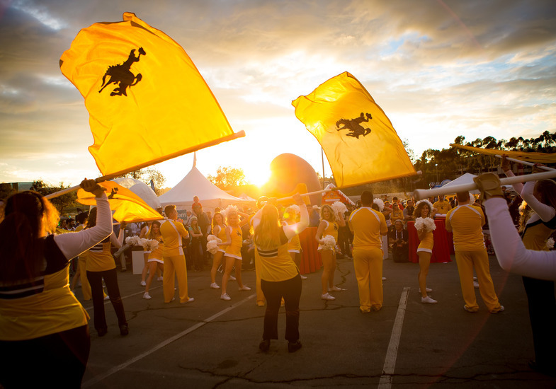 Group of color guard members spinning flags behind UW Spirit Squad as the sun sets.