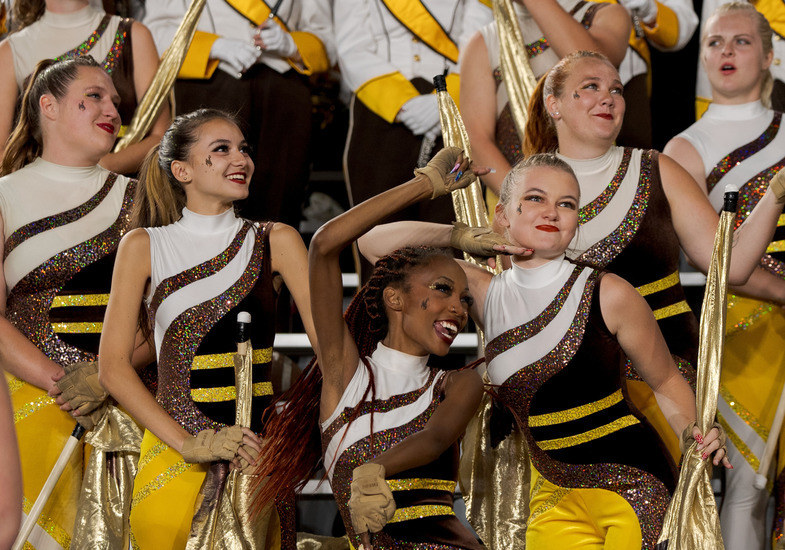 Group of women in color guard uniforms smiling and dancing at a football game.