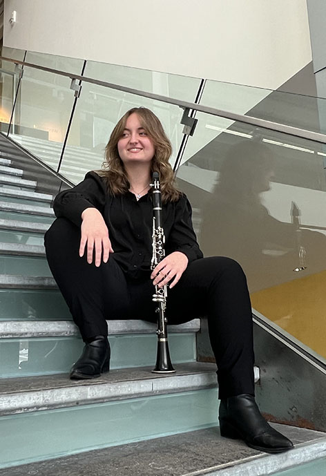 Picture of person smiling while sitting on stairs holding a clarinet, wearing all black.