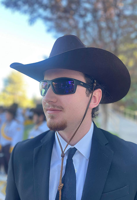 Image of person in suit, cowboy hat and sunglasses looking to the side of camera.