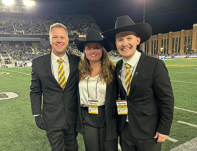 Photo of WTMB director and graduate assistants smiling at a football game.