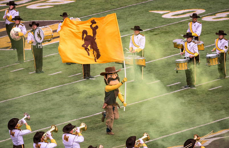 Pistol Pete running down the football field during gameday between members of Western Thunder Marching Band.