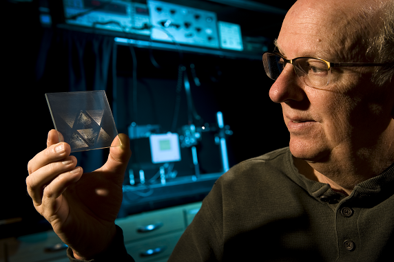 Photo of a man with glasses in a lab looking at a translucent image on a piece of glass