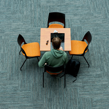 Looking down from a story above on a student in the College of Business Atrium on his computer