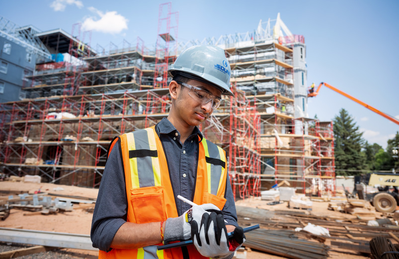 mechanical engineering student standing in front of a construction site using a tablet
