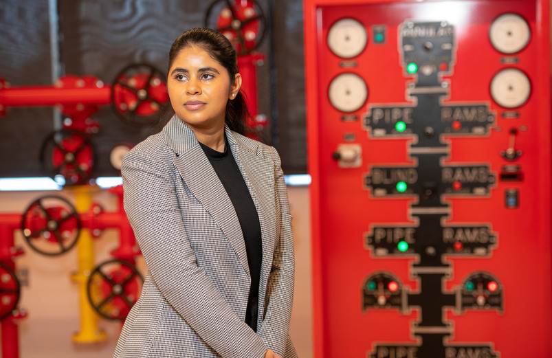 A petroleum engineering student standing in front of guages at an energy facility