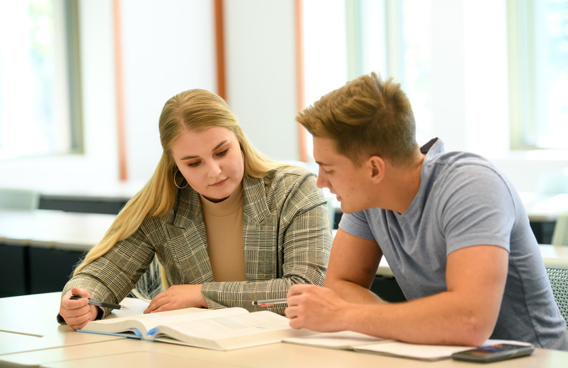 Two College of Business students looking at a book and a notebook in a College of Business conference room