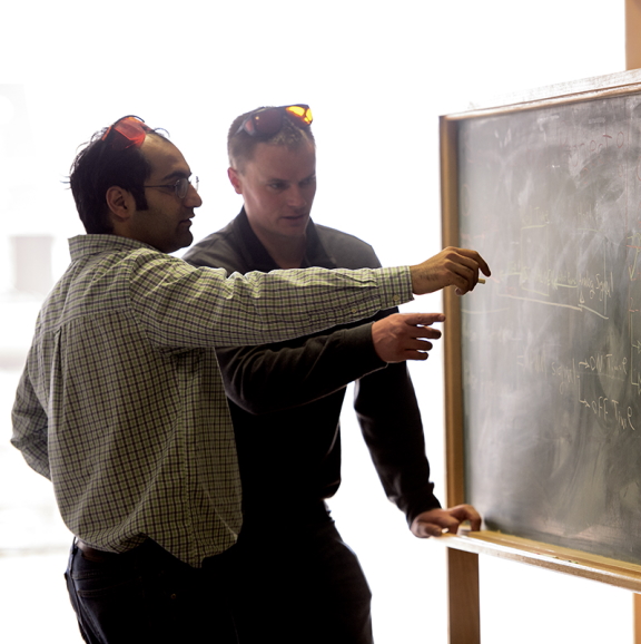 Graduate students discussing formulas in front of chalkboard