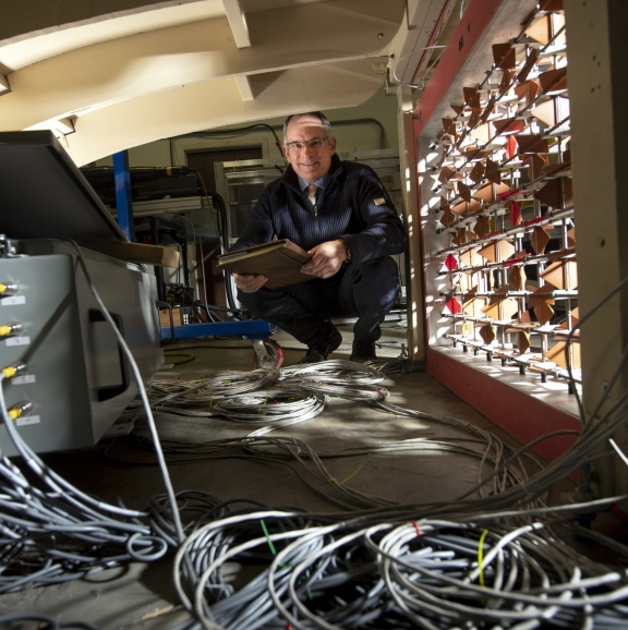 Professor Jonathan Naughton kneeling in his lab with many cables in the foreground