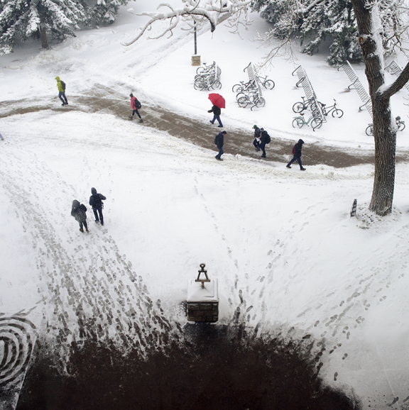 Photo from an upper story window overlooking a statue of THE BENT with students walking in the snow