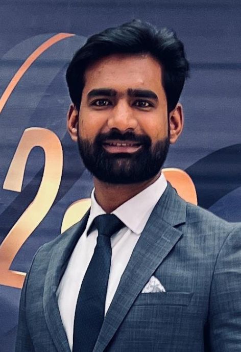 photo of Ikram Arif, wearing a grey suit in front of a navy and gold backdrop