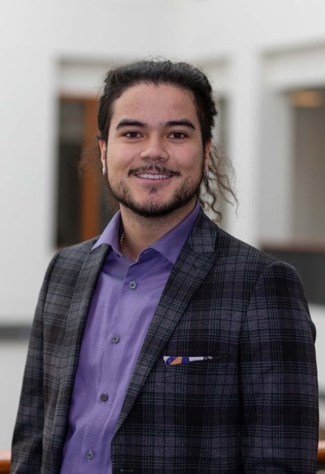 candid photo of kasen arriola wearing a a greay plaid suit jacket over a lavender shirt.